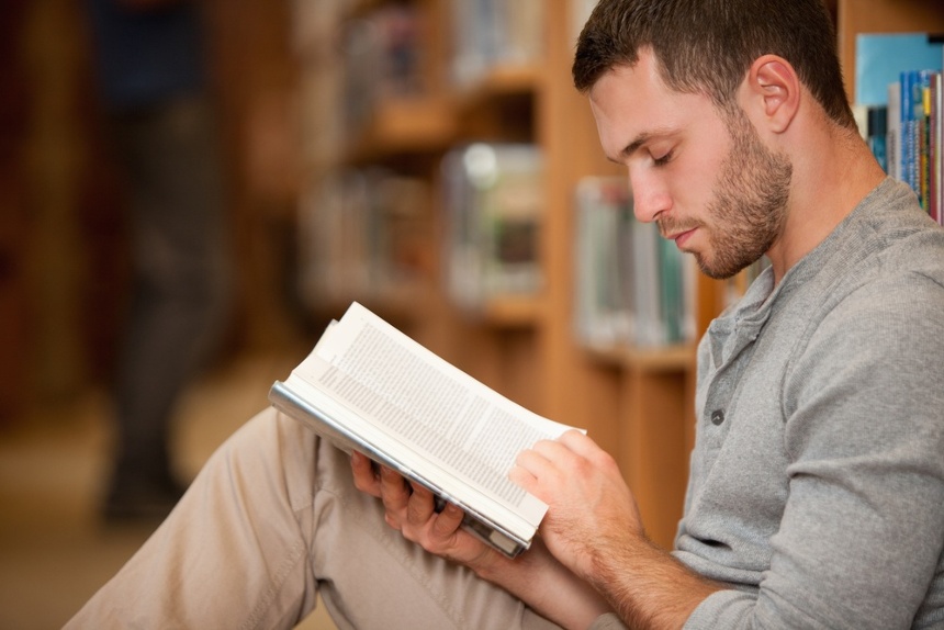 Serious male student reading a book in a library