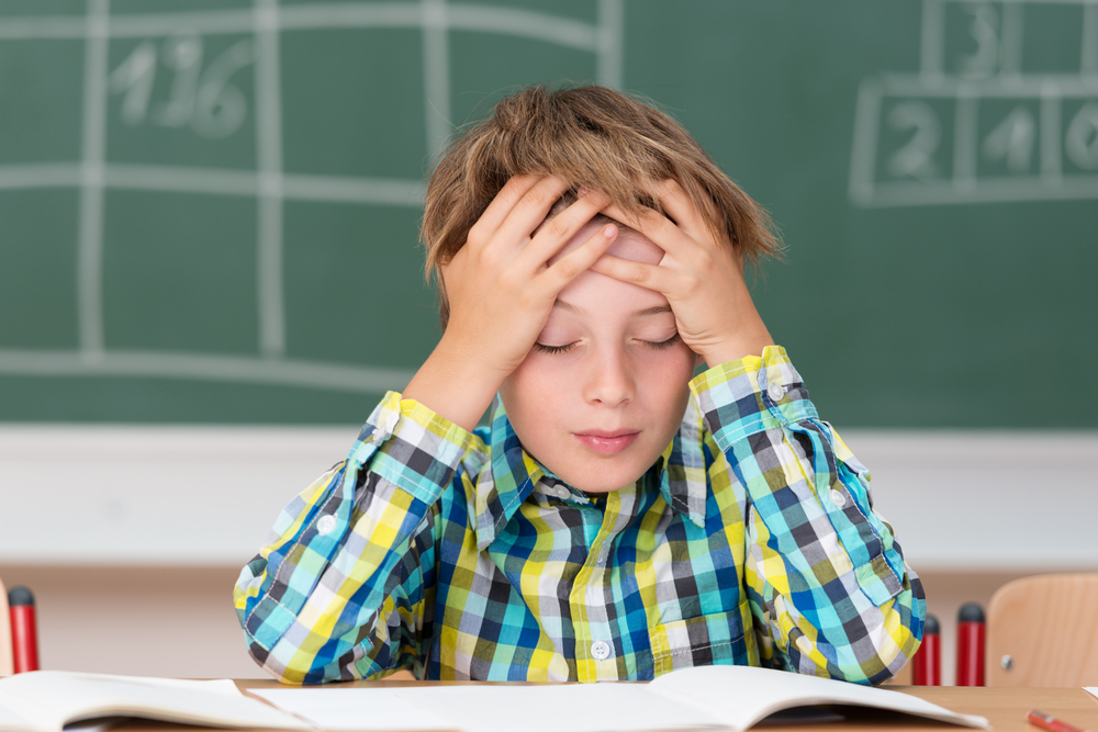 Young boy concentrating on his schoolwork sitting at his desk in the classroom with his head in his hands reading his class notes Young boy concentrating on his schoolwork sitting at his desk in the classroom with his head in his hands reading his class notes